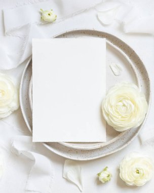 Krem güllerin yanında kart ve beyaz ipek kurdeleler olan düğün masası, üst manzara, maket. Dikey kart ve pastel çiçeklerle romantik bir sahne. Sevgililer Günü, Bahar veya Anneler Günü konsepti