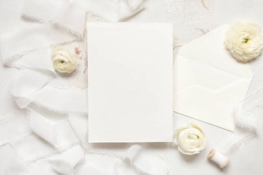 Krem güllerin yanındaki boş kart ve beyaz ipek kurdeleler üst manzara, düğün modeli. Dikey kart ve pastel çiçeklerin düz olduğu romantik bir sahne. Sevgililer Günü, Bahar veya Anneler Günü konsepti
