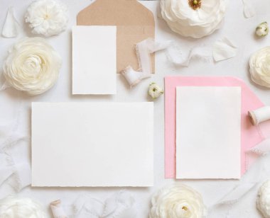 Krem güllerin yanında boş kartlar ve zarflar ve beyaz ipek kurdeleler. Düğün seti ve pastel çiçeklerle romantik bir sahne. Sevgililer Günü, Bahar veya Anneler Günü konsepti