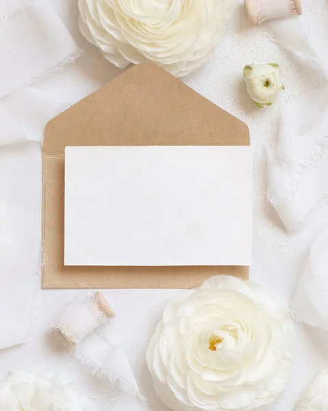 在奶油玫瑰和白色丝带旁边的空白卡片和信封可以看到 浪漫的婚礼场景与横向卡片和油腻的花朵平铺 情人节或春天的概念 — 图库照片