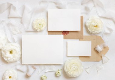 Krem güllerin yanında boş kartlar ve zarflar ve beyaz ipek kurdeleler. Düğün seti ve pastel çiçeklerle romantik bir sahne. Sevgililer Günü, Bahar veya Anneler Günü konsepti