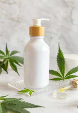 Yeşil kenevir sativa yakınlarındaki beyaz bir pompa şişesi, kavanozlar ve pipetler mermer masa manzaralı. Mockup, uzayı kopyala. Organik cilt bakım ürünü. Çevre dostu CBD Kozmetik ve Oi