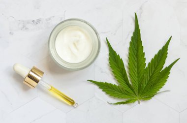 CBD yağlı boru ve beyaz mermer masa manzaralı yeşil kenevir yapraklarının yanında krema kavanozu açıldı. Organik cilt ürünleri, doğal kozmetik ürünleri.