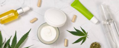 Mermer masa manzaralı yeşil kenevir sativa yapraklarının yanında boş etiketli krema şişeleri, kavanozlar ve tüpler. Mockup, uzayı kopyala. Organik cilt ürünleri. CBD Kozmetik