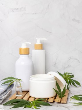 Yeşil kenevir yapraklarının yanında boş kapaklı krema kavanozu diğer şişelerin yanındaki banyoda, ahşap tepside, yakın plan, maket. Organik cilt ürünleri, doğal CBD kozmetik ürünleri