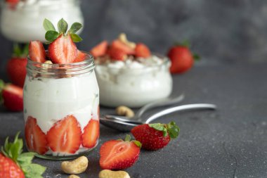 Yunan yoğurdu, fındık ve çilek cam bir kavanozda gri beton bir masada kaşık ile, yakın çekim, kopyalama alanı. Meyve ve fındıklı sağlıklı kahvaltı. Protein yemek için harika bir yol.