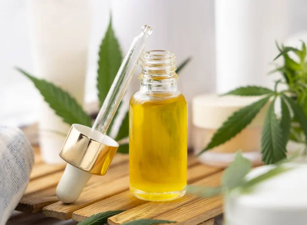 Opened Dropper bottle with CBD oil and green cannabis leaves near bottles and towel close up in bathroom. Organic healthcare product. Alternative medicine and cosmetic