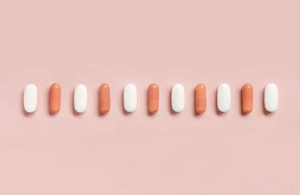 Mix of medical capsules in a line on light pink top view. Preventive medicine and healthcare, dietary supplements and vitamins.  Assorted pharmaceutical medicine capsules