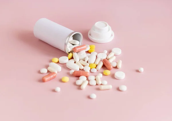 Mix of medical capsules and pills with a bottle on light pink top view. Medicinal treatment. Taking dietary supplements and vitamins. Assorted pharmaceutical products