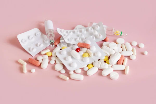Mix of medical capsules and pills with blisters on light pink top view. Medicinal treatment. Taking dietary supplements and vitamins. Assorted pharmaceutical products