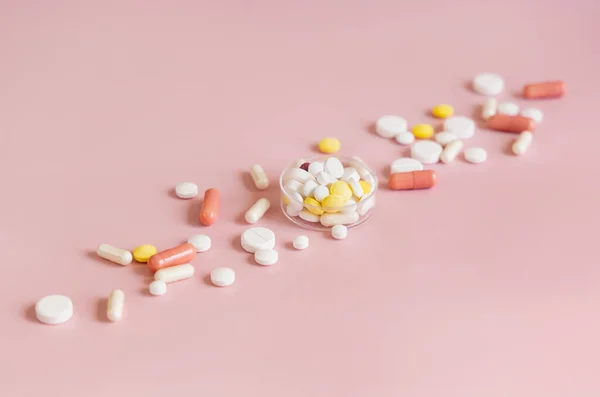 Medical pills and capsules in a bowl on light pink close up.  Taking dietary medicines, supplements and vitamins. Assorted pharmaceutical products