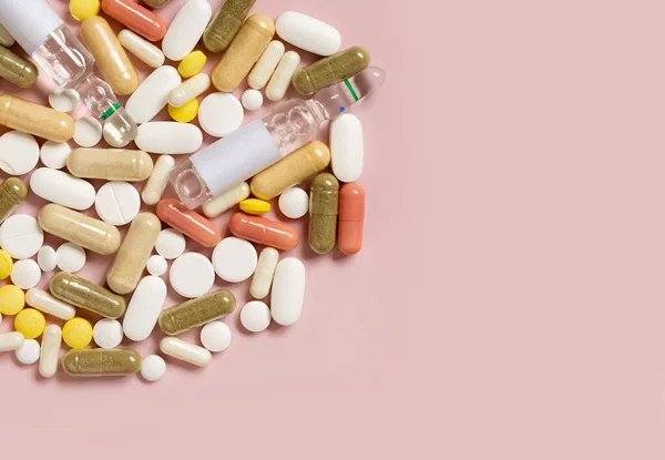 Mix of medical capsules and pills on light pink top view, copy space. Medicinal treatment. Taking dietary supplements and vitamins. Assorted pharmaceutical products