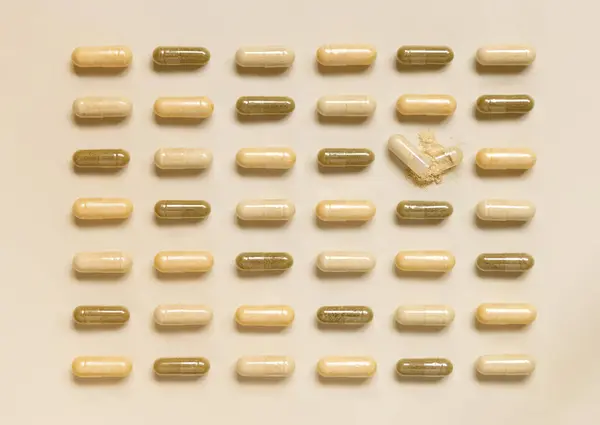 Mix of beige and brown medical capsules in  lines on light beige top view. Preventive medicine and healthcare, dietary supplements and vitamins.  Assorted pharmaceutical medicine capsules
