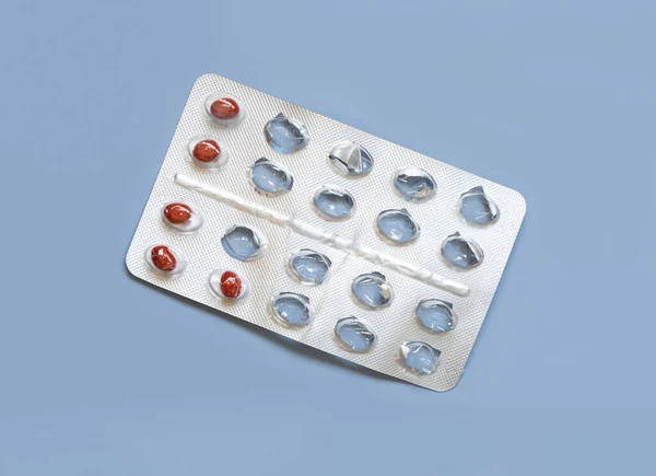 Red pills in a aluminum and plastic blister with some missing pills already used on light blue top view. Medicine and healthcare, taking dietary supplements and vitamins