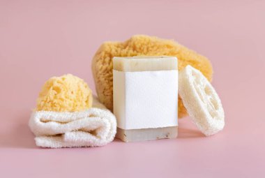 Boş etiketli bej el yapımı sabun, doğal süngerler ve açık pembe üzerine havlu yakın çekim, ambalaj modeli, kopyalama alanı. Yüz ve vücut bakımı için bitkisel ürünler