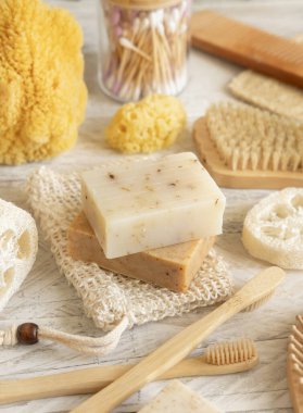 Doğal süngerler, bambu diş fırçaları ve pamuklu çubuklar gibi hijyen malzemelerinin yanında sabun koruyucu poşetlerinde bulunan organik el yapımı bej sabunlar. Doğal bitkisel ürünler