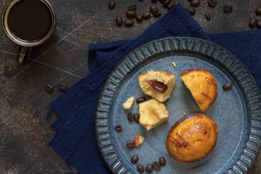 Kahve fincanının yanında koyu mavi bir tabakta Pasticciotto leccese hamur işi ve koyu masa üzerinde moka, tipik apulian kahvaltısı, üst manzara. Kahve çekirdekleri ve peçeteyle süslenmiş bir masa.