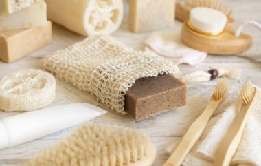 Doğal süngerler, bambu diş fırçaları ve pamuklu çubuklar gibi hijyen malzemelerinin yanında sabun tasarruf poşetinde bulunan organik el yapımı bej bir sabun. Doğal bitkisel ürünler