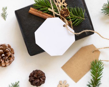 Köknar ağacı dalları, çam kozalakları ve tatil süslemeleri ile Noel hediyesi etiketi ile kaplanmış siyah bir hediye. Boş Hediye Etiketi ile Rustik kış kompozisyonu, kopyalama alanı, kapat