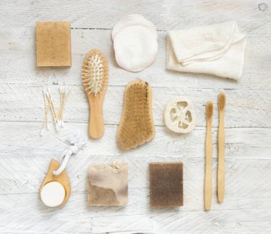 Sabun çubukları ve doğal hijyen ürünleri beyaz ahşap masa üzerinde üst görünüm. Havlu, doğal sünger ve fırça, bambu diş fırçası ve pamuk çubukları, üst manzara.