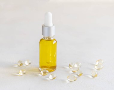 Sarı yağ damlatan şişede ve kapsüller beyaz bir masada. Koruyucu ilaçlar ve sağlık hizmetleri, beslenme takviyeleri ve vitaminler