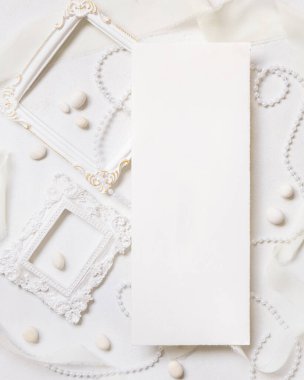 Beyaz çerçeveler, inciler, çakıl taşları ve beyaz masa manzaralı ipek kurdeleler, düğün menüsü modeli. Düz kartın olduğu romantik bir sahne. Sevgililer Günü, Bahar veya Anneler Günü konsepti