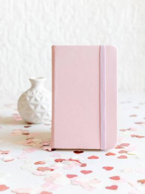 Kalplerin yanında pembe kaplı defter ve beyaz masaya yakın vazo. Düğün, Sevgililer Günü, Bahar veya Anneler Günü için romantik bir model. 