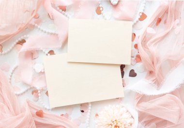 Kağıt kartlar pembe dekorasyonlar, kalpler ve beyaz masa manzaralı ipek kurdeleler, maket. Yatay olarak boş kartların olduğu romantik bir sahne. Düğün, Sevgililer Günü, Bahar veya Anneler Günü kırtasiyesi