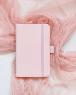 Beyaz masa manzaralı tül kumaş üzerine pembe kaplı defter. Romantik bir model. Eğitim ve Okula Dönüş konsepti