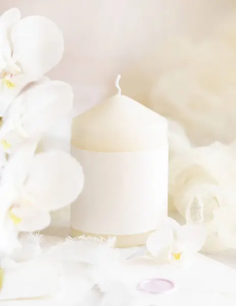 Homemade pillar candle with a blank label near white orchid flowers and tulle close up,  mockup.  Brand packaging mock up. Home decoration, romantic interior