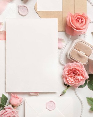 Açık pembe güllerin yanındaki boş kart, bir kutuda nişan yüzüğü ve beyaz masa manzaralı ipek kurdeleler, düğün modeli. Dikey Kart ve Pastel Dekorlu Romantik Düz 