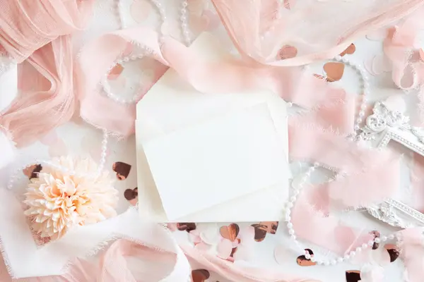 空白卡片和信封旁边的粉红饰品 红心和丝带上的白色桌子顶部视图 浪漫的平铺与水平空白卡片 情人节或春季文具 — 图库照片