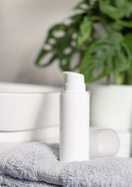 Белый качающий косметический флакон на сером складном инструменте возле таза и зеленый монстр в ванной крупным планом, косметический макет. Современная сцена жизни с женским средством личной гигиены