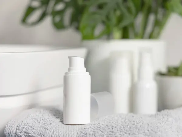 White one pump cosmetic bottle on grey folded towel near basin and green monstera in bathroom close up, cosmetic mockup. Modern lifestile scene with female personal care product