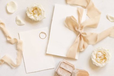 Kartlar beyaz masa manzaralı bej ipek bir kurdeleyle bağlanmış. Düğün kırtasiyesi modeli. Dikey boş kartlarla, güllerle ve yüzüklerle romantik bir sahne. Düğün ya da Sevgililer Günü kırtasiyesi