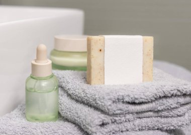 Açık yeşil kozmetik şişeleri ve kavanozların yanında boş etiketli sabun kalıbı, ambalaj maketi, kopyalama alanı. Kadın güzellik rutini için doğal hijyen ürünleri