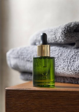 Banyodaki kahverengi ahşap tezgahın üstündeki leğen üzerinde gri katlanmış havlunun yanındaki yeşil damlacık şişesi, yakın çekim, marka ambalajı için kozmetik model.