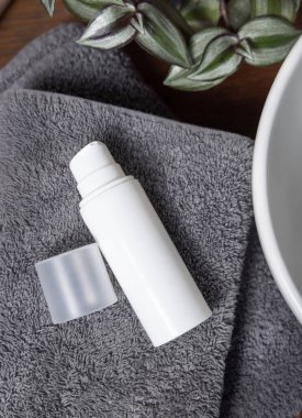 Beyaz pompa krem şişesi gri havlular üzerinde yeşil bitki yanında kahverengi ahşap tezgah banyoda, üst manzara, marka ambalaj modeli. Doğal el yapımı kozmetik ürünü