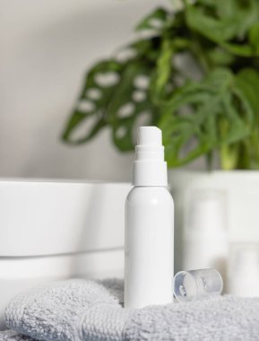 Havuzun yanındaki gri katlı havlunun üzerine beyaz sprey makyaj spreyi ve banyoda yeşil canavar, kozmetik maketi. Kadın kişisel bakım ürünleriyle modern yaşam sahnesi