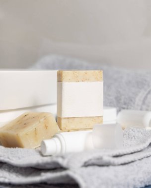 Havza, açık gri havlular ve kapalı krem şişeler, kozmetik maketi olan bej bir sabun barı. Tuvalette hijyen ve kişisel bakım ürünleriyle dolu hayat dolu bir sahne.