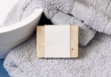 Damarın yanında açık gri havlular üzerinde boş etiketli bej sabun barı lavabo, yakın plan, marka ambalaj modeli. Doğal el yapımı hijyen ürünü.