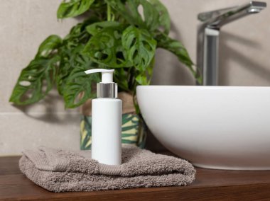 Beyaz olan havlunun yanında kahverengi katlanmış havluya kozmetik şişesi banyoda ahşap tezgahta yeşil canavara ise makyaj malzemesi pompalıyor. Sürdürülebilir kişisel bakım ürünleriyle modern yaşam sahnesi