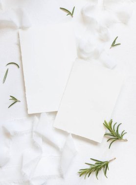 Beyaz ipek kurdelelerin yanındaki boş kartlar ve biberiye yaprakları üst manzara, düğün modeli. Dikey kartlar ve aromatik yaprakların düz olduğu romantik bir sahne. Sevgililer Günü, Bahar veya Anneler Günü konsepti