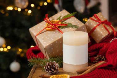 Noel hediyesinin yanında boş etiketli sütun mumu, kurutulmuş meyveler, kırmızı süveter ve Noel ağacı ışıklarına yakın köknar dalları, fotokopi alanı. Sıcak kış aile atmosferi. Tatil zamanı.