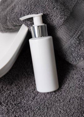 Koyu gri havlular üzerinde beyaz krem pompa şişesi banyodaki damar havlusunun yanında, yakın çekim, ambalaj modeli. Doğal el yapımı kozmetik ürünü