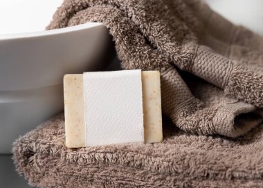 Açık kahverengi havluların üzerinde boş etiketi olan bej sabun barı banyoda lavabo, yakın plan, marka ambalaj modeli. Doğal el yapımı hijyen ürünü.