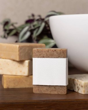 Yeşil bitkinin yanında boş etiketli sabun barı ve banyoda kahverengi ahşap tezgahın üzerinde kap kaplama, marka ambalaj modeli. Erkekler için hijyen ürünü