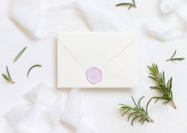 Beyaz ipek kurdeleler ve biberiye yapraklarının yanında boş bir zarf. Üst manzara, düğün modeli. Dikey kartlar ve aromatik yaprakların düz olduğu romantik bir sahne. Sevgililer Günü, Bahar veya Anneler Günü konsepti