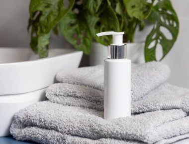 Beyaz olan havuzun yanında açık gri katlanmış havluyla kozmetik şişesi pompalıyor ve banyoda yeşil bitki, kozmetik modelleme. Kişisel bakım ürünü, krem ya da losyon içeren hayat dolu bir sahne