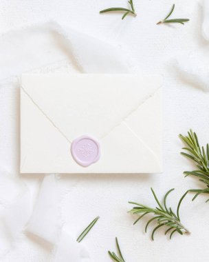 Beyaz ipek kurdeleler ve biberiye yapraklarının yanında boş bir zarf. Üst manzara, düğün modeli. Dikey kartlar ve aromatik yaprakların düz olduğu romantik bir sahne. Sevgililer Günü, Bahar veya Anneler Günü konsepti